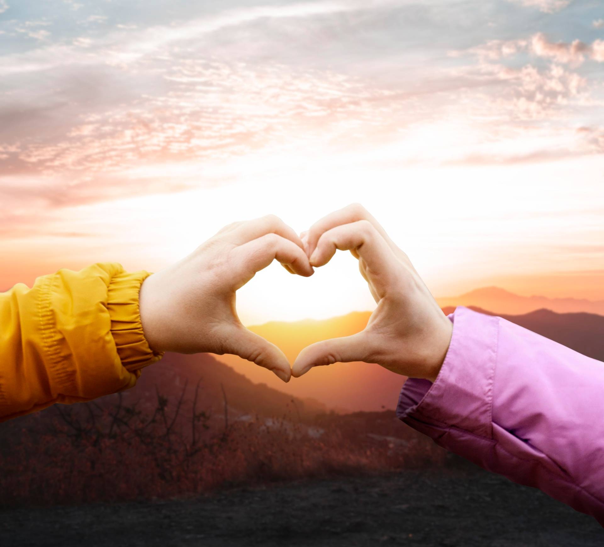 Two hands forming a heart shape against a sunset background.